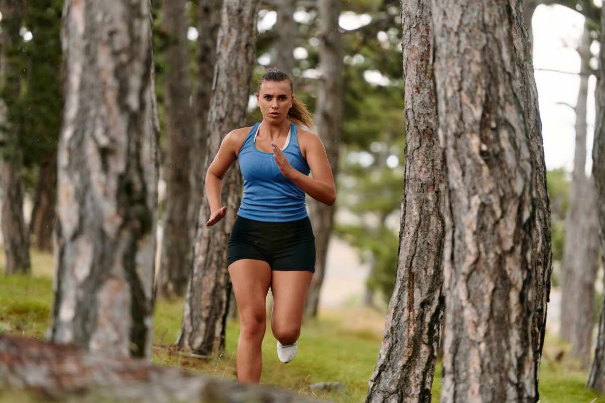 Mujer corriendo entre árboles altos.